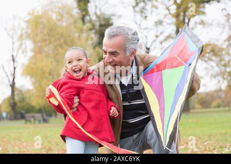 Verspielter Großvater und Enkelin fliegen im Herbstpark einen Drachen Stockfoto