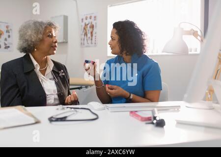 Hausärztin unterrichte Oberpatientin, wie man Glukosimeter in der Arztpraxis verwendet Stockfoto