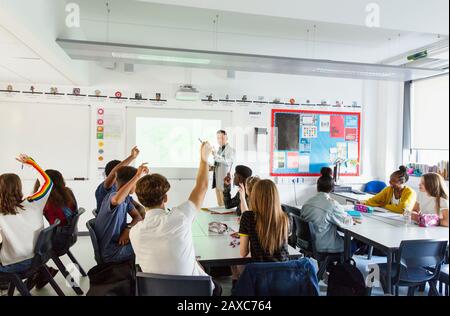 Die High-School-Lehrerin ruft die Schüler mit erhobenen Händen während des Unterrichts im Klassenzimmer auf Stockfoto