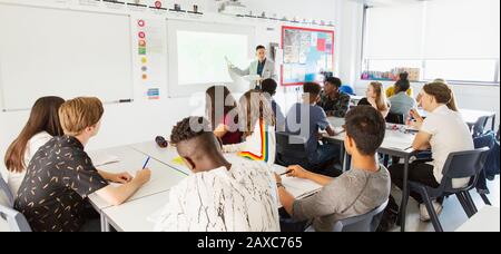 Schüler der High School, die Lehrer während des Unterrichts im Klassenzimmer auf der Projektionsleinwand beobachten Stockfoto