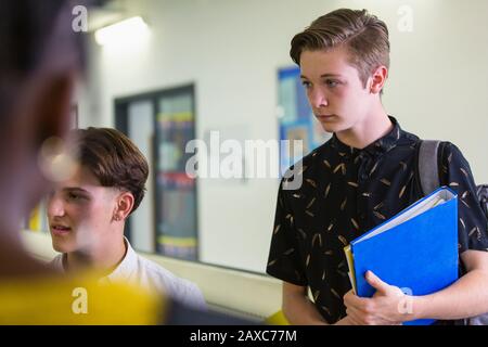 Konzentrierter Schüler mit hohem Jungen, der Freunde auf Korridor hört Stockfoto