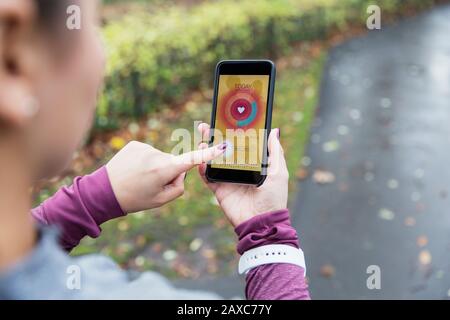 Laufbuchse, die den Herzfrequenzsensor auf dem Smartphone auf dem Pfad überprüft Stockfoto
