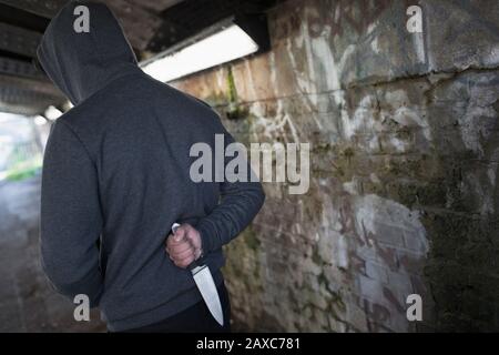 Gefährlicher Mann mit Messer hinter dem Rücken im städtischen Tunnel Stockfoto