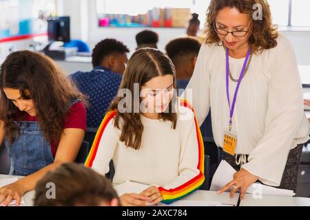 Weibliche High-School-Lehrerin, die Mädchen dabei hilft, Hausaufgaben im Klassenzimmer zu machen Stockfoto