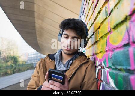 Junger Mann mit Kopfhörern, der Musik auf städtischen Bürgersteigen hört Stockfoto