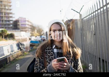 Porträt lächelnde junge Frau mit Smartphone auf städtischem Bürgersteig Stockfoto