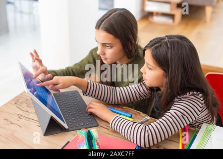 Schwestern, die Hausaufgaben machen und digitales Tablet am Tisch teilen Stockfoto