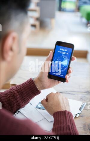 Mann, der sich mit Gesichtserkennung beim Smartphone anmeldet und Rechnungen online bezahlt Stockfoto