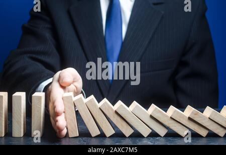 Der Geschäftsmann stoppt den Sturz des Domino. Strategieentwicklung. Umstrukturierung der Schulden. Konzept des Risikomanagements. Zuverlässiger Marktführer. Stoppen Sie die zerstörerischen Prozesse. Stockfoto