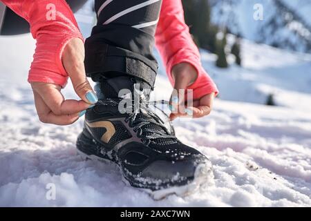 Junge Frau, die Laufschuh bindet, um das Joggen auf dem Winter-Bergpfad auf Schnee vorzubereiten Stockfoto