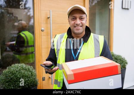 Portrait selbstbewusster, freundlicher Lieferer mit Paket und Smartphone vor der Haustür Stockfoto