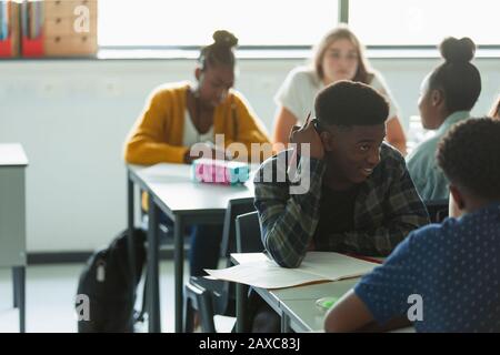 Schüler der High School machen Hausaufgaben und sprechen an Tischen im Klassenzimmer Stockfoto
