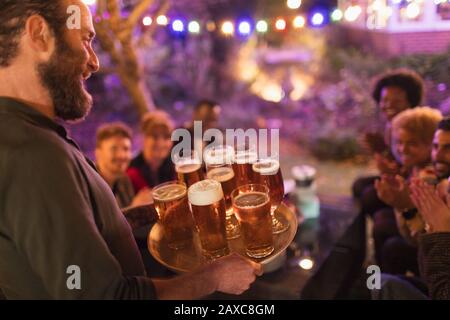 Mann, der auf der Gartenparty ein Tablett Bier für Freunde serviert Stockfoto