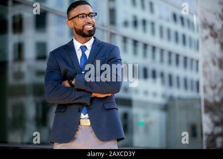 Gutaussehender CEO von African american Business man in einem Anzug am Arbeitsplatz, selbstbewusst mit gefalteten Armen stehend Stockfoto