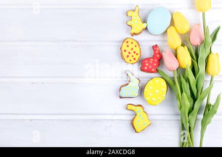 Gelbe Tulpen und Oster-Lebkuchen-Plätzchen auf weißem Holztisch. Frühlings- oder Osterferienkonzept, Kopierraum, flaches Lay, Vorlagenmockup-Begrüßung Stockfoto