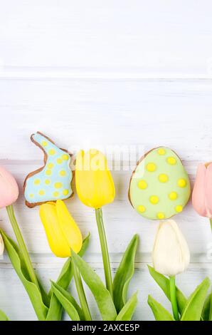Gelbe Tulpen und Oster-Lebkuchen-Plätzchen auf weißem Holztisch. Frühlings- oder Osterferienkonzept, Kopierraum, flaches Lay, Vorlagenmockup-Begrüßung Stockfoto