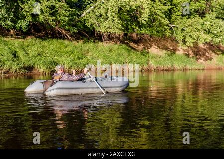 Ein Mann fängt Fische auf dem Fluss, ein Fischer auf einem Gummiboot schwimmt auf dem Fluss Stockfoto