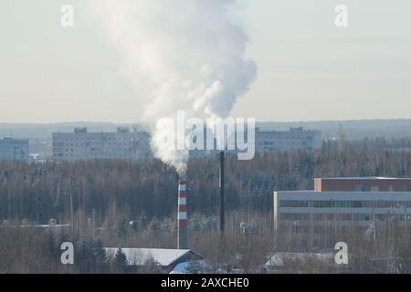 Rauchwolke steigt aus dem indastrischen Schornstein vor dem wolkenigen Himmel auf. Indastridalzone in der Stadt Russland. Winterliches Stadtbild mit Gebäuden und Park. Stockfoto mit leerem Textbereich. Stockfoto