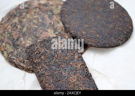 Gepresste Pfannkuchen und Ziegelsteinform mit Blick auf den Tee. Chinesische Puer Shu und shen in Form von Pfannkuchen 100, 250, 357 Gramm. Traditioneller Tee für Teezubereiter Stockfoto