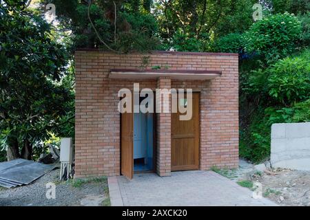 Ein kleines Gebäude in einem Park mit zwei Türen. die toilette im Botanischen Garten ist aus Backstein auf einem Baumhintergrund angelegt. Roter Ziegelbau in einem p Stockfoto