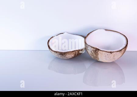 Zwei Hälften Kokosnuss liegen auf glattem hellem Hintergrund. Tropisches Obst neutraler, eleganter Hintergrund. Gesunder frischer Koko mit Kopierraum. Stockfoto