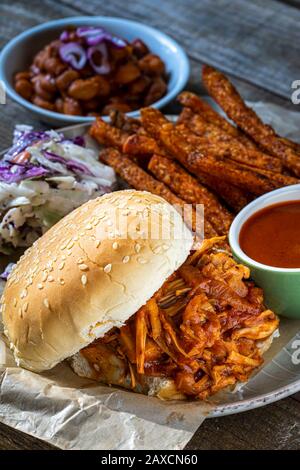 Veganes BBQ-Sandwich. Grill-Jack-Fruit mit süßen Kartoffelfries, süßen gebackenen Bohnen und Coleslaw. Stockfoto