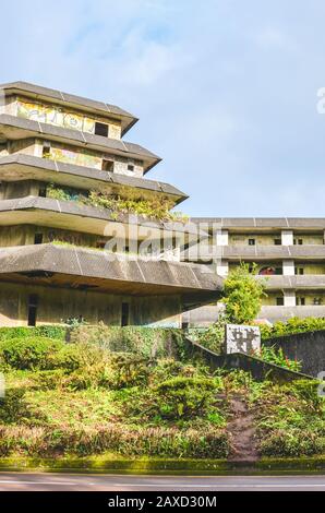 Sete Cidades, Azoren, Portugal - 12. Januar 2020: Verlassenes Hotelgebäude auf dem berühmten Aussichtspunkt auf den portugiesischen Inseln. Leerbetonbau von außen. Grüne Bäume um. Stockfoto