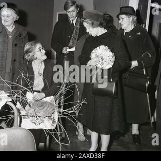 In den 1960er Jahren traf Mrs. Wison, die Ehefrau des britischen Premierministers Harold Wilson, auf eine Bewohnerin eines alten Wohnhauses in South London, England, Großbritannien, sitzend und machte einen Korb. Stockfoto