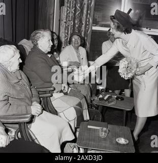 1960er Jahre, historisch, Mrs. Wison, die Ehefrau des britischen Premierministers Harold Wilson, grüßt die weiblichen Bewohner eines Altershauses bei einem Besuch in South London, England, Großbritannien. Eine unprätentiöse, bescheidene Frau, die angeblich Gedichte, Blumen und die einfachen Freuden des Heim- und Familienlebens liebte, unterstützte ihren Mann bei fünf allgemeinen Wahlen und lebte ein langes Leben von 102 Jahren. Stockfoto