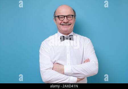 Glücklicher ranghoher hispanischer Kahlmann in einer Brille, der mit gefalteten Händen auf der Kamera lächelt. Studio gedreht Stockfoto