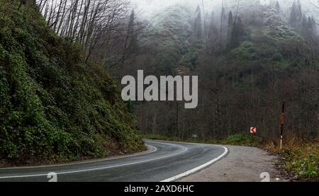 In der Wintersaison eine nasse Straße zwischen den Hügeln biegen. Stockfoto