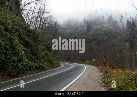 In der Wintersaison eine nasse Straße zwischen den Hügeln biegen. Stockfoto