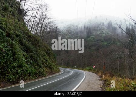 In der Wintersaison eine nasse Straße zwischen den Hügeln biegen. Stockfoto