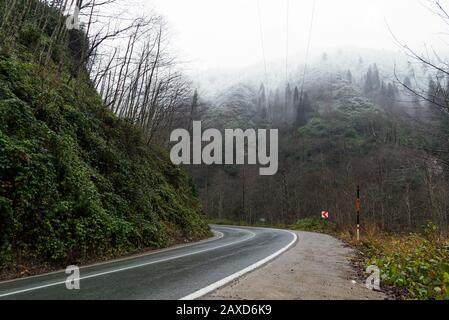 In der Wintersaison eine nasse Straße zwischen den Hügeln biegen. Stockfoto