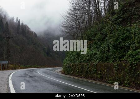 In der Wintersaison eine nasse Straße zwischen den Hügeln biegen. Stockfoto