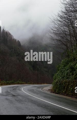 In der Wintersaison eine nasse Straße zwischen den Hügeln biegen. Stockfoto