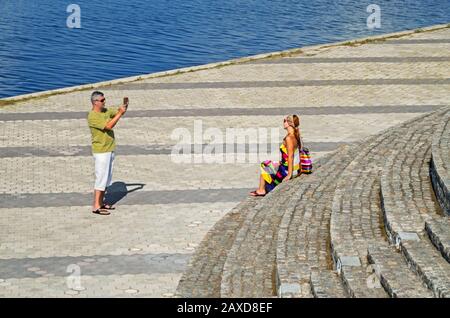 Dnipro, Ukraine - 10. August 2016: Ein Mann fotografiert Frau auf der Promenade mit einem Handy am sonnigen Tag Stockfoto