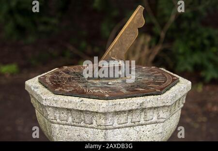 Ein traditionelles Gartenherz, eine bronzene Sonnenuhr auf einem geschnitzten Steinsockel. 5-Minuten-Schritte. Zeitmessung. Stockfoto