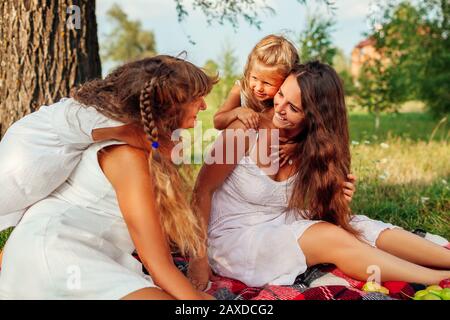 Muttertag, Frauentag. Frau und ihre Kinder mit Großmutter umarmend. Familie mit Picknick im Park Stockfoto