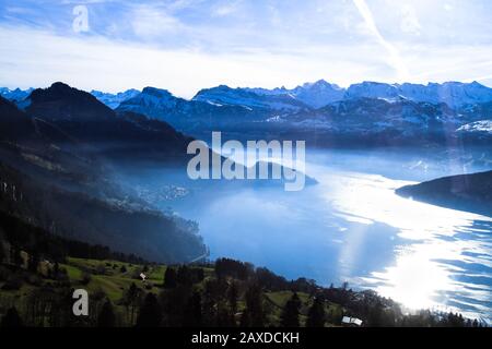 Panaramische Skyline Blick auf schneebedeckte Berge, die unvornehmlich über den nebligen Vierwaldstattersee, Vitznau, den Luzerner See, Schweiz, ragen, von insid genommen Stockfoto