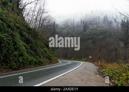 In der Wintersaison eine nasse Straße zwischen den Hügeln biegen. Stockfoto