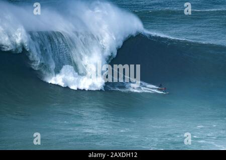 Surfer Andrew Cotton (UK) in Rot und Alex Botelho (POR) in Schwarz werden während der Surfchallenge von Nazaré Tow am Strand Praia do Norte auf einer Welle reiten gesehen. In Nazaré.Nazaré Tow Surfing Challenge ist ein großer Wellenwettbewerb der World Surf League, der am Strand Praia do Norte stattfand. Es nutzte den riesigen Schwell, der am 11. Februar an die portugiesische Küste traf. Stockfoto