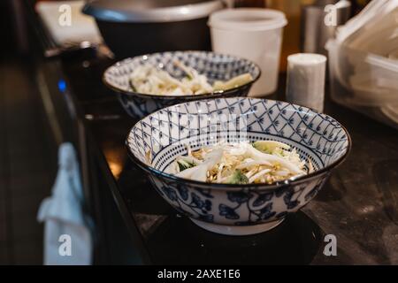 Ausgewählte Fokusansicht, Zubereitung von Reisnudel, Bohnenspriet und Gemüse in Schüsseln mit chinesischem blauem Muster, auf der Theke in der Küche des Restaurants. Stockfoto