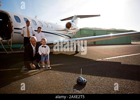 Großvater, der seinen Enkel beobachtet, spielt mit einem Spielzeugauto, während er an einem Flugzeug steht Stockfoto