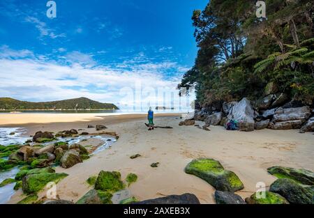 Junge Frau am Strand mit moosbedeckten Felsen, Stillwell Bay, Bach Lesson Creek, Abel Tasman Coastal Track, Abel Tasman National Park Stockfoto