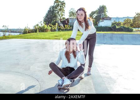 Zwei Teenager-Mädchen, 12-14 Jahre alte Schulmädchen, im Sommer in der Stadt, reiten Skateboard, lächeln glücklich und haben Spaß am Jubeln. Wochenendpause. Freizeit Stockfoto