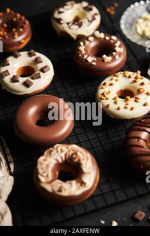 Vertikale Aufnahme von köstlichen Donuts in der weißen und bedeckt Braune Schokoladenglasur auf einem schwarzen Tisch Stockfoto