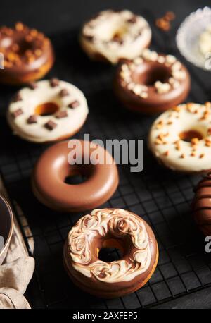 Vertikale Aufnahme von köstlichen Donuts in der weißen und bedeckt Braune Schokoladenglasur auf einem schwarzen Tisch Stockfoto