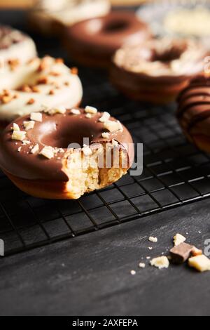 Vertikale Aufnahme von köstlichen Donuts in der weißen und bedeckt Braune Schokoladenglasur auf einem schwarzen Tisch Stockfoto