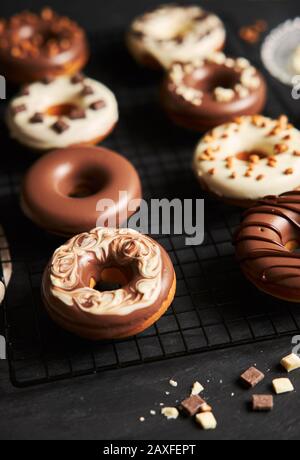 Vertikale Aufnahme von köstlichen Donuts in der weißen und bedeckt Braune Schokoladenglasur auf einem schwarzen Tisch Stockfoto